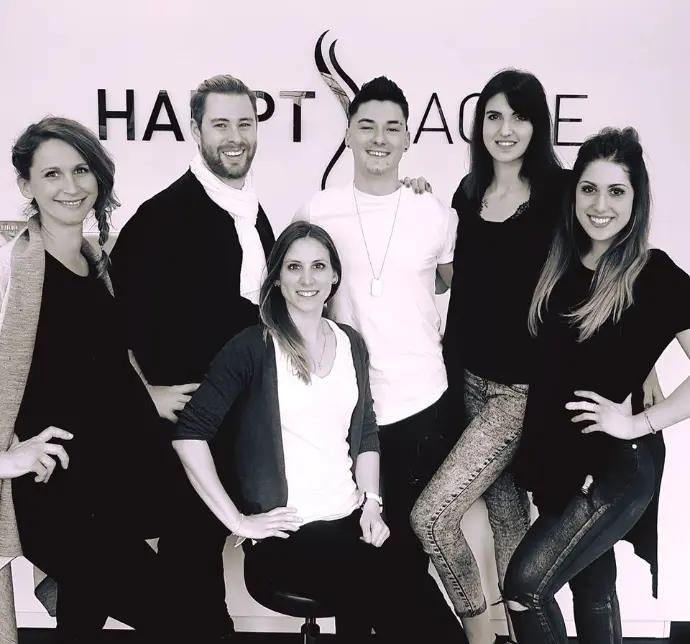 Schwarz-weiß Gruppenfoto des Teams von Coiffeur HAUPTSACHE Sursee vor dem Salon-Logo